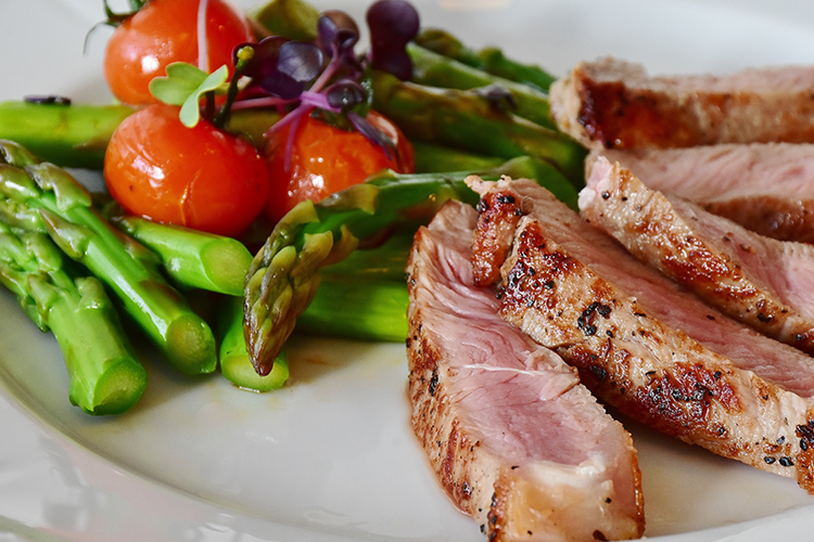 a prepared dinner of meat, asparagus, and tomatoes