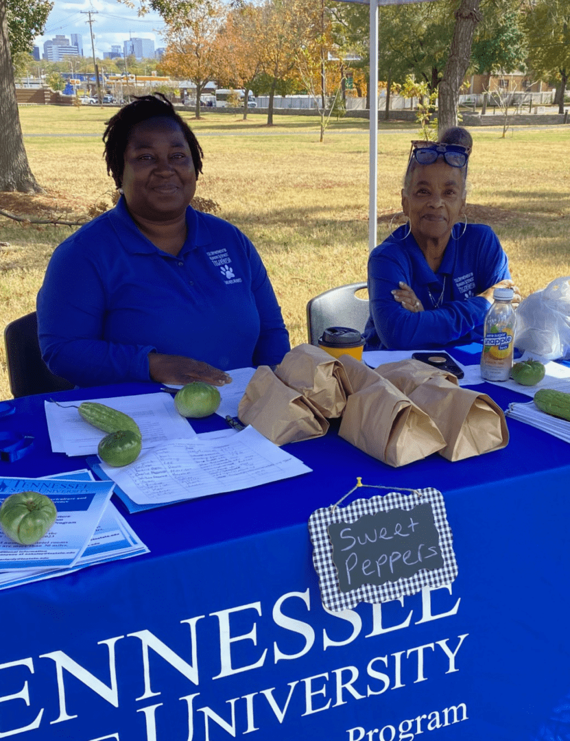 two Tennessee State University employees smiling. They are sitting at a table with vegetables