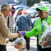 an Extension employee hands a community member a bag of fresh produce