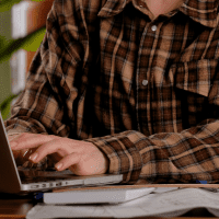 a person in a flannel types on a laptop