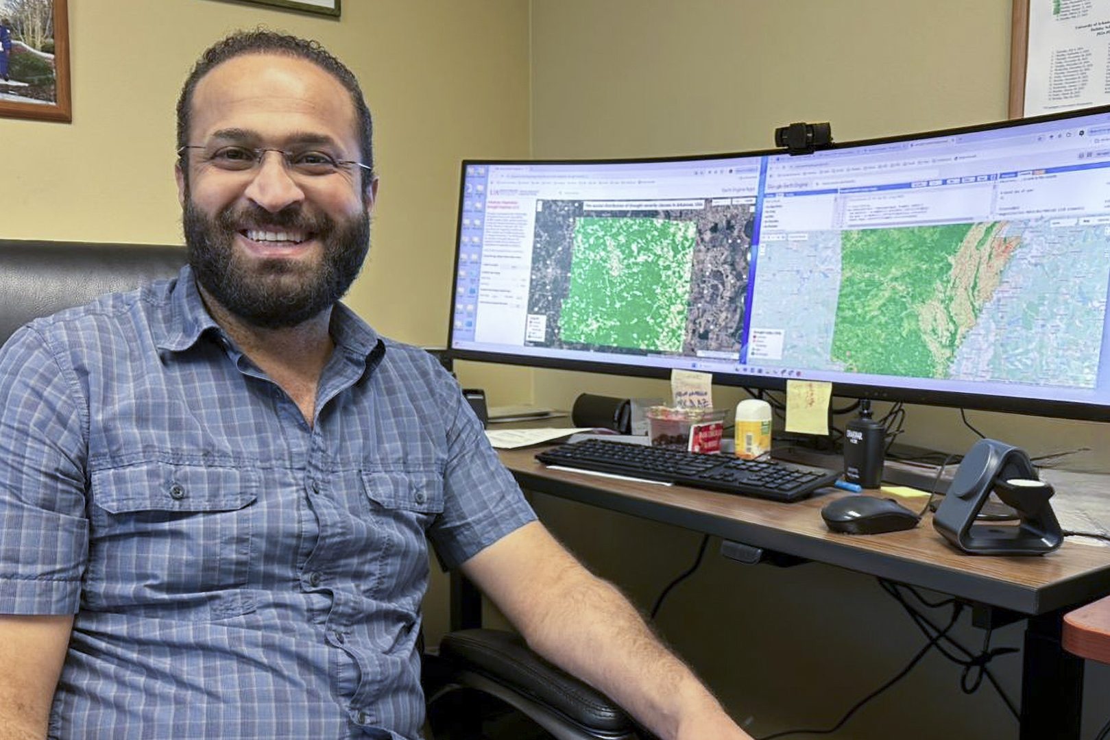 Hamdi Zurqani sits next to wide computer monitor showing the Arkansas Vegetation Drought Explorer.