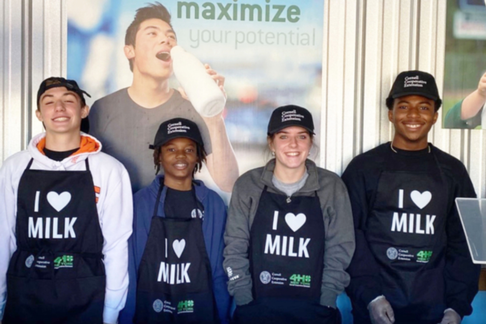 Youth workers pose before promotional posters at the 2023 Milk Bar in the Dairy Building at the Great New York State Fair